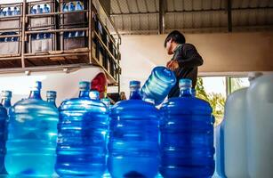 Arbeitskräfte Aufzug Trinken Wasser klar und sauber im Blau Plastik Gallone in das zurück von ein Transport LKW gereinigt Trinken Wasser Innerhalb das Produktion Linie zu bereiten zum Ausverkauf.klein Geschäft foto