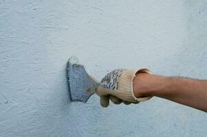 ein Hand im ein Arbeit Handschuh Farben das Mauer von das Haus mit Blau malen. foto