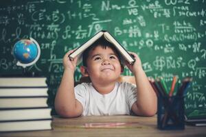 nachdenklicher kleiner Junge mit Buch im Klassenzimmer foto