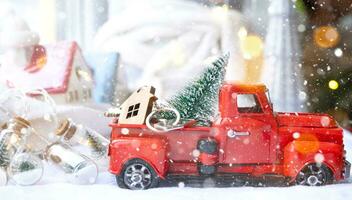 Rotes Retro-Auto mit einem Weihnachtsbaum schmückt mit dem Hausschlüssel im Pickup-Truck zu Weihnachten. Hauskauf, Umzug, Hypothek, Darlehen, Immobilien, Feststimmung, Neujahr foto