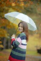 asiatisch jünger Frau mit Regen Regenschirm Glück lächelnd Gesicht Fleckenbildung im Japan Herbst Park foto