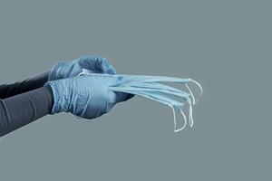 Hände im Einweg Handschuhe halten medizinisch Maske auf ein grau Hintergrund. Foto mit Kopieren Raum.