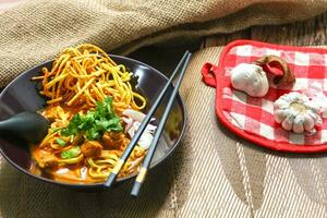 Nudeln mit Schweinefleisch und Gemüse im ein Schüssel auf das Tisch, khao soi Kai, Nord Stil Curry Nudel Suppe mit Wahl von eingelegt Hähnchen foto