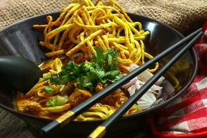 Nudeln mit Schweinefleisch und Gemüse im ein Schüssel auf das Tisch, khao soi Kai, Nord Stil Curry Nudel Suppe mit Wahl von eingelegt Hähnchen foto