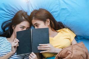 Süßes asiatisches lesbisches Paar, das zusammen ein Buch liest und auf dem Bett liegt foto
