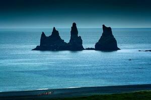 Reynisdragar natürlich Felsen Formation auf atlantisch Ozean und Gruppe von Tourist Reiten Pferde Besichtigung auf das schwarz Sand Strand im Sommer- beim Island foto