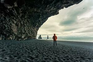 reynisdrangar natürlich Felsen Formation mit weiblich Tourist Stehen im halsanefshellir Höhle auf schwarz Sand Strand im Sommer- beim Island foto