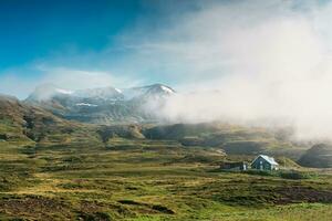 Aussicht von ländlich Szene mit skandinavisch Haus auf Berg und winzig Wasserfall im nebelig auf Sommer- beim Island foto