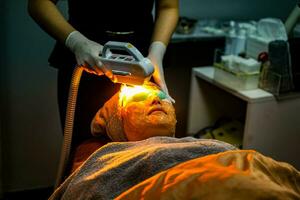 Nahansicht asiatisch Schönheit Frau Empfang Laser- Behandlung durch Fachmann Kosmetikerin Wohlbefinden im Schönheit Klinik. foto