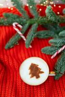 Weihnachten Komposition gemacht von norwegisch Nobilis Kiefer und dekoriert mit Beleuchtung und Süßigkeiten Stöcke im das bilden von ein Stock. ein Tasse von Cappuccino mit ein Weihnachten Baum Muster. Weihnachten und Neu Jahr Konzept. foto
