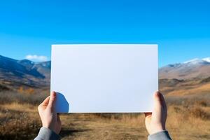 Hand gehaltenen leer Landschaft Papier gegen schön Berg und Blau Himmel Hintergrund, ai generiert foto