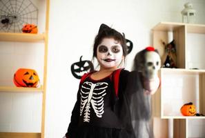 Porträt asiatisches kleines Mädchen im Halloween-Kostüm, das den Schädel hält foto