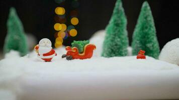 Weihnachten Spielzeug auf Girlande Hintergrund. Spielzeug Santa claus auf das Hintergrund von Licht Glühbirnen. Weihnachten Hintergrund Santa claus mit ein Geschenk. foto