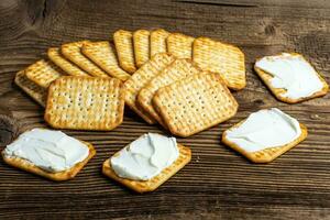 mit Käse bestrichene Cracker als leichter Snack auf einem Holzbrett foto