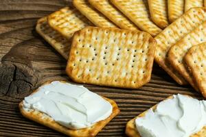 mit Käse bestrichene Cracker als leichter Snack auf einem Holzbrett foto