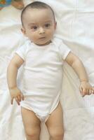 6-8 Monate alt Baby Junge Lügen spielerisch im Bett. charmant 6-7 Monat wenig Baby im Weiß Body. Baby Junge im Weiß Bettwäsche. Kopieren Raum foto