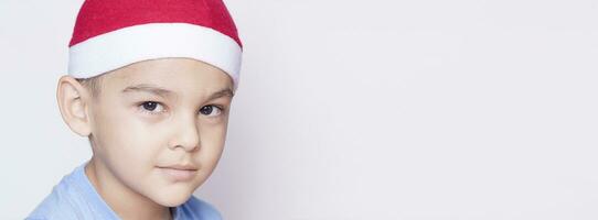 Porträt von ein sechsjährig Junge gegen das Weiß Hintergrund. feiern Weihnachten. 6-7 Jahr alt Kind mit Santa Hut. foto