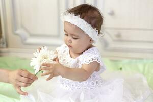 Baby Mädchen im Weiß Kleid nehmen ein schön Single Weiß Blume foto