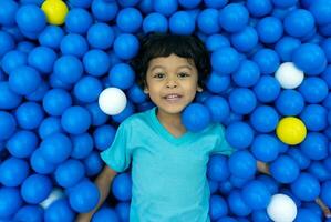 ein wenig asiatisch Junge ist spielen mit ein Menge von Blau und Gelb Bälle foto