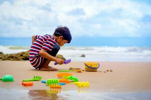 wenig asiatisch Junge abspielen mit Sand auf das Strand. foto
