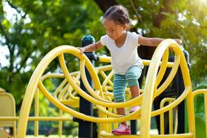 asiatisch Mädchen ist Klettern auf ein Spielplatz Ausrüstung im ein Schule. foto