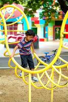 asiatisch Junge ist Klettern auf ein Spielplatz Ausrüstung im ein Schule. foto