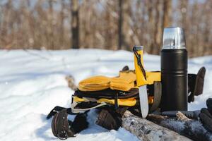 ein Messer zum Überleben im das Wald ist stecken mit ein Klinge in ein Protokoll. Tourist Ausrüstung, Ausrüstung zum ein Winter Wanderung, ein Thermosflasche mit heiß Tee. foto