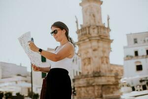 weiblich Tourist mit Stadt Karte durch das Heilige oronzo Statue im Ostuni, Italien foto