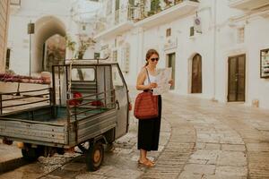 weiblich Tourist mit Papier Stadt Karte auf eng Straßen von Ostuni, Italien foto