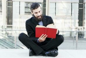 junger Hipster, der ein Buch liest, das draußen sitzt foto