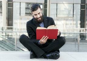 junger Hipster, der ein Buch liest, das draußen sitzt foto
