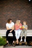 Familie mit ein Mutter, Vater und Tochter Sitzung draußen auf das Schritte von ein Vorderseite Veranda von ein Backstein Haus foto