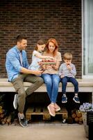 Familie mit ein Mutter, Vater, Sohn und Tochter Sitzung draußen auf Schritte von ein Vorderseite Veranda von ein Backstein Haus und Essen Erdbeeren foto