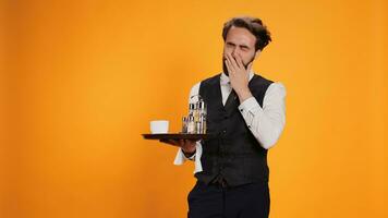 erschöpft Diener Gefühl schläfrig auf Kamera, Gähnen und fallen schlafend auf Pflicht beim Restaurant. Bedienung im formal Kleidung Gefühl müde und Dehnen im Studio, Stehen gegen Gelb Hintergrund. foto