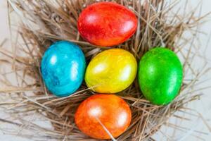 mehrfarbig Ostern Eier Lüge zusammen auf ein Stroh im das bilden von ein Nest auf ein Weiß Hintergrund. glücklich Ostern foto
