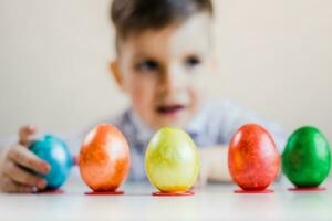 mehrfarbig Ostern Eier Stand im ein Reihe auf steht auf ein Tabelle gegen das Hintergrund von ein süß Junge. foto