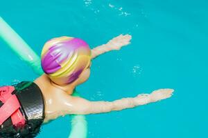 ein wenig Junge mit ein Leben Jacke auf seine Truhe lernt zu schwimmen im ein Innen- Schwimmbad. foto