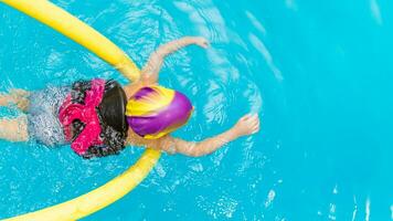 ein wenig Junge mit ein Leben Jacke auf seine Truhe lernt zu schwimmen im ein Innen- Schwimmbad. foto