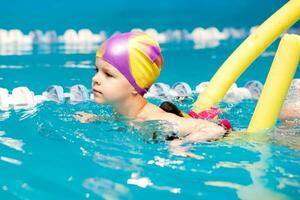 ein wenig Junge mit ein Leben Jacke auf seine Truhe lernt zu schwimmen im ein Innen- Schwimmbad. foto