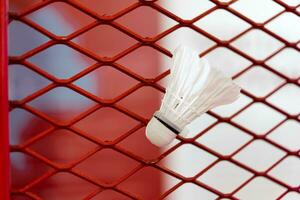 Federbälle wurden stecken zu das Badminton Stahl Grill Netz mit ein groß rot Zeichnung von Federball auf Hintergrund neben. foto