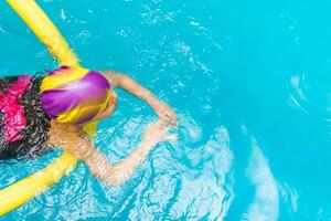 ein wenig Junge mit ein Leben Jacke auf seine Truhe lernt zu schwimmen im ein Innen- Schwimmbad. foto