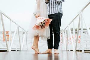 Füße von das Jungvermählten auf das Seebrücke. Beine von das Braut und Bräutigam barfuß auf das Kai. foto