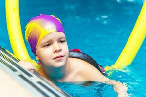 ein wenig Junge mit ein Leben Jacke auf seine Truhe lernt zu schwimmen im ein Innen- Schwimmbad. foto