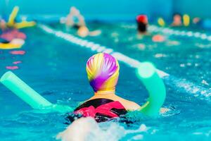 ein wenig Junge mit ein Leben Jacke auf seine Truhe lernt zu schwimmen im ein Innen- Schwimmbad. foto