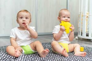 süß glücklich Babys abspielen zusammen auf das Fußboden mit Spielzeuge und nehmen Sie im ihr Münder foto