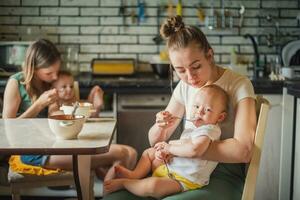zwei müde aber glücklich Mütter Futter ihr Babys Milch Haferbrei im das Küche foto