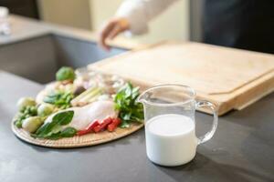 Kokosnuss Sahne ,Milch, ist enthalten im ein groß Messung Tasse neben ein Gruppe von Essen Zutaten und diese Produkte ist im Vorderseite von ein Holz Schneiden Tafel. foto