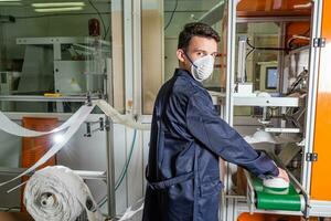 ein Mann funktioniert beim ein Maschine zum das Herstellung von medizinisch Masken mit Nanofaser. Coronovirus und covid-19 Verhütung foto