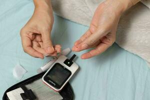 ein Frau Hand Überprüfung ihr Blut Zucker Niveau mit ein Glukometer durch Sie selber beim ihr heim. ShotlistGesundheit foto