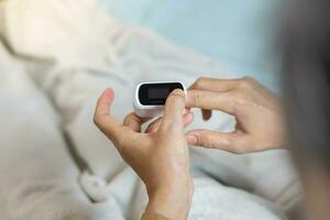 weiblich Hände mit ein Impuls Oximeter beim das Index Finger. Frau Lügen beim das Bett. Gadgets zum Gesundheit Pflege. Konzept von Entschlossenheit von Sauerstoff im das Blut. ShotlistGesundheit foto